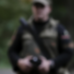 description: an anonymous image depicts a man with a blurred face wearing military attire, holding a firearm.