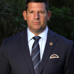 description: a headshot of ron desantis wearing a suit and tie, with a serious expression on his face.