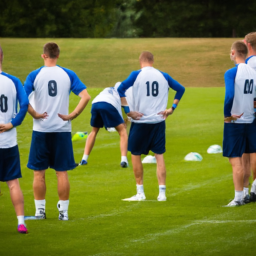 description: a group of football players in blue and white jerseys practicing on a lush green field, with a coach giving instructions in the background. the players are focused and determined, showcasing their skills in anticipation of the upcoming friendly matches.